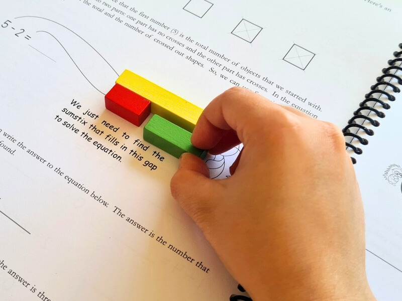 Milestone maths hands-on math manipulatives with a child working out a problem in a maths workbook