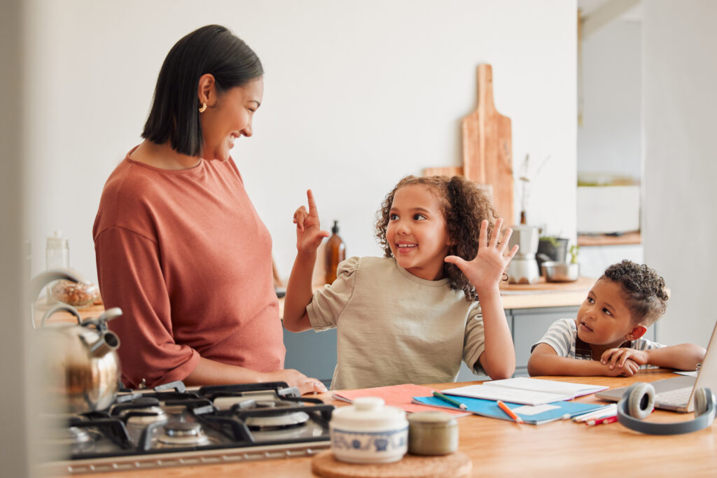 A mother smiling, teaching and helping children with maths work in the kitchen. Mum and kids using the internet to homeschool her young daughter and son, to help with maths, for a happy family and kids using Maths Vault lessons and activities