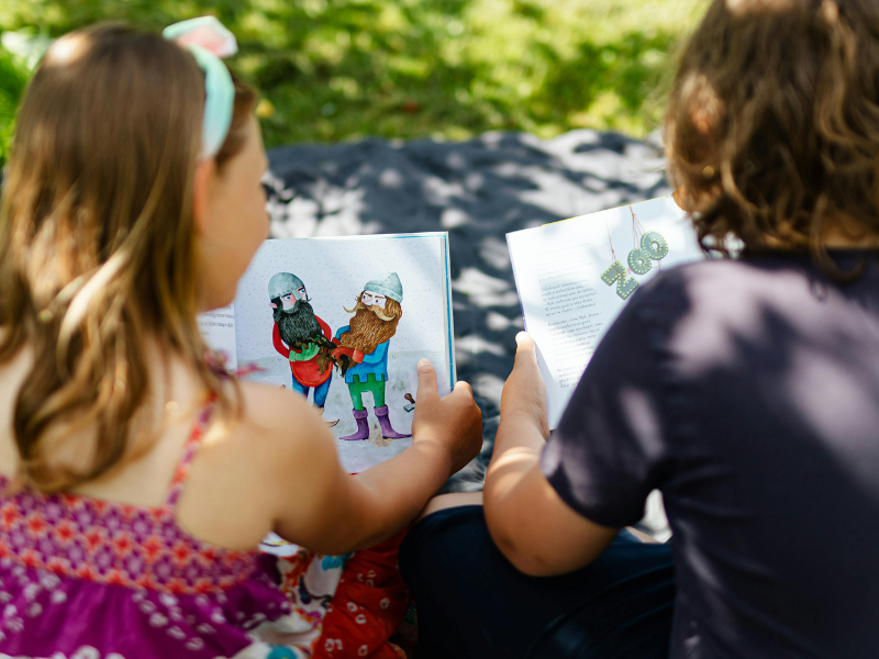 homeschool children reading books on a picnic blanket outdoors